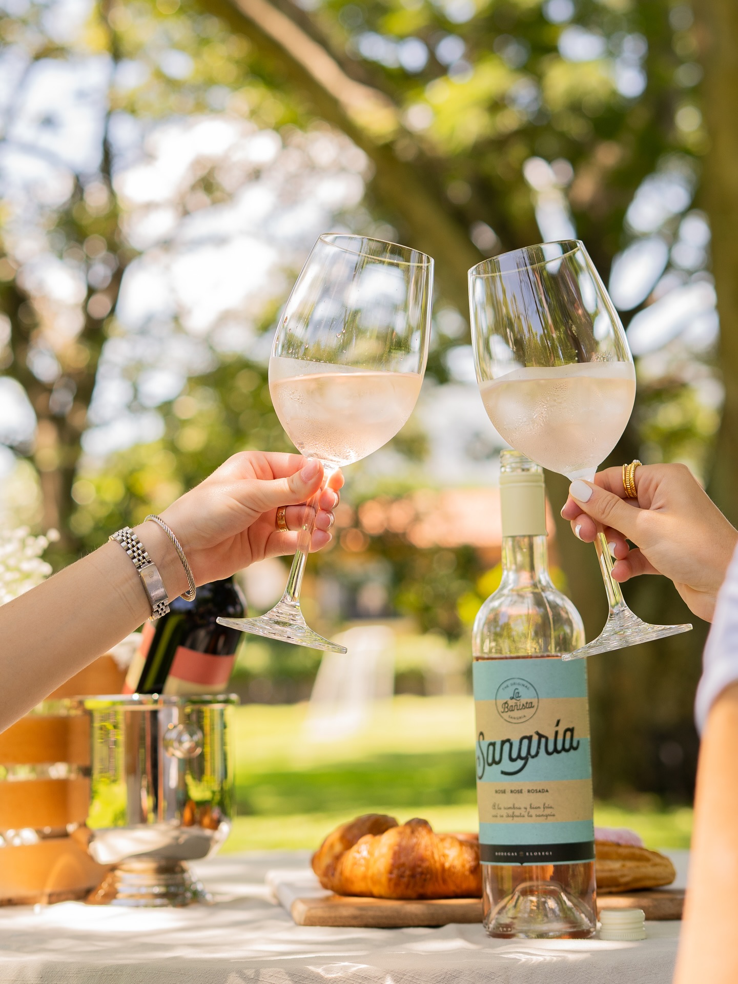Dos personas brindan con copas de sangría junto a una botella de La Bañista